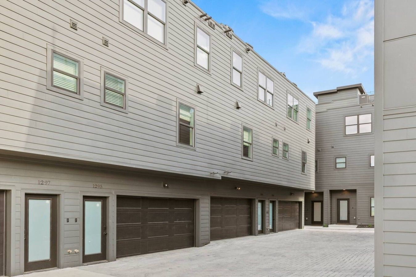 A multi-story residential building with a flat facade, multiple garage doors, and a clear sky.