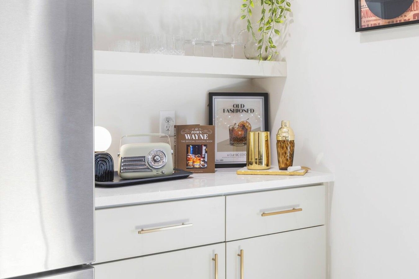 A kitchen counter with a vintage radio, a cocktail book, a cocktail shaker, and a bottle of liquor.