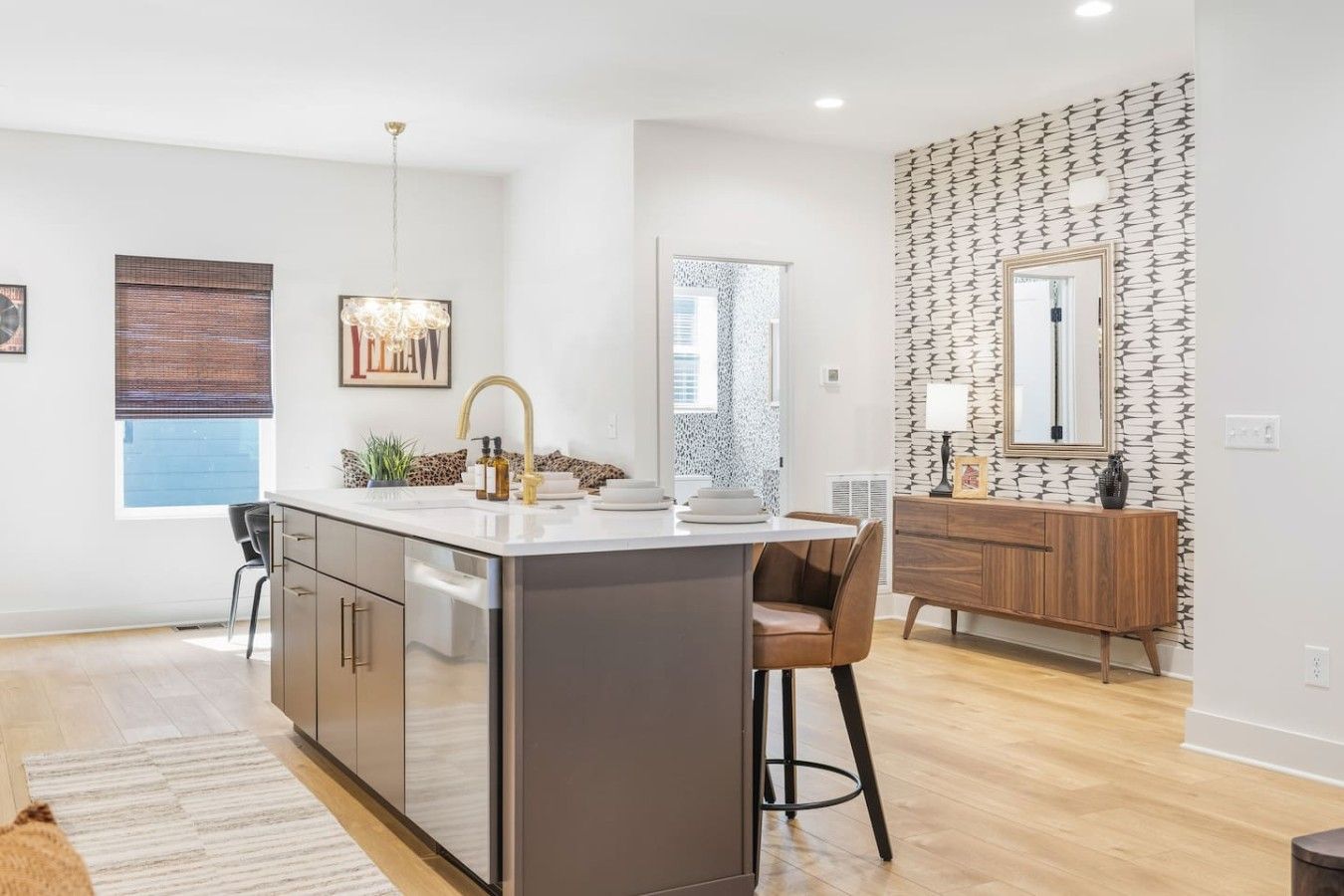A modern kitchen with a central island, a dining area with a chair, and a wooden console table with a mirror.
