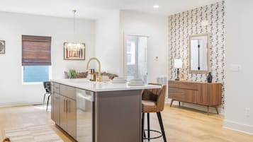 A modern kitchen with a central island, a dining area with a chair, and a wooden console table with a mirror.
