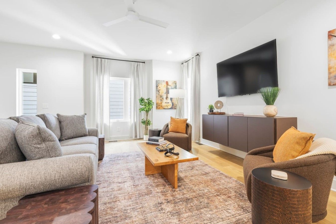 A modern living room with a sofa, armchair, coffee table, and a flat-screen TV mounted on the wall.