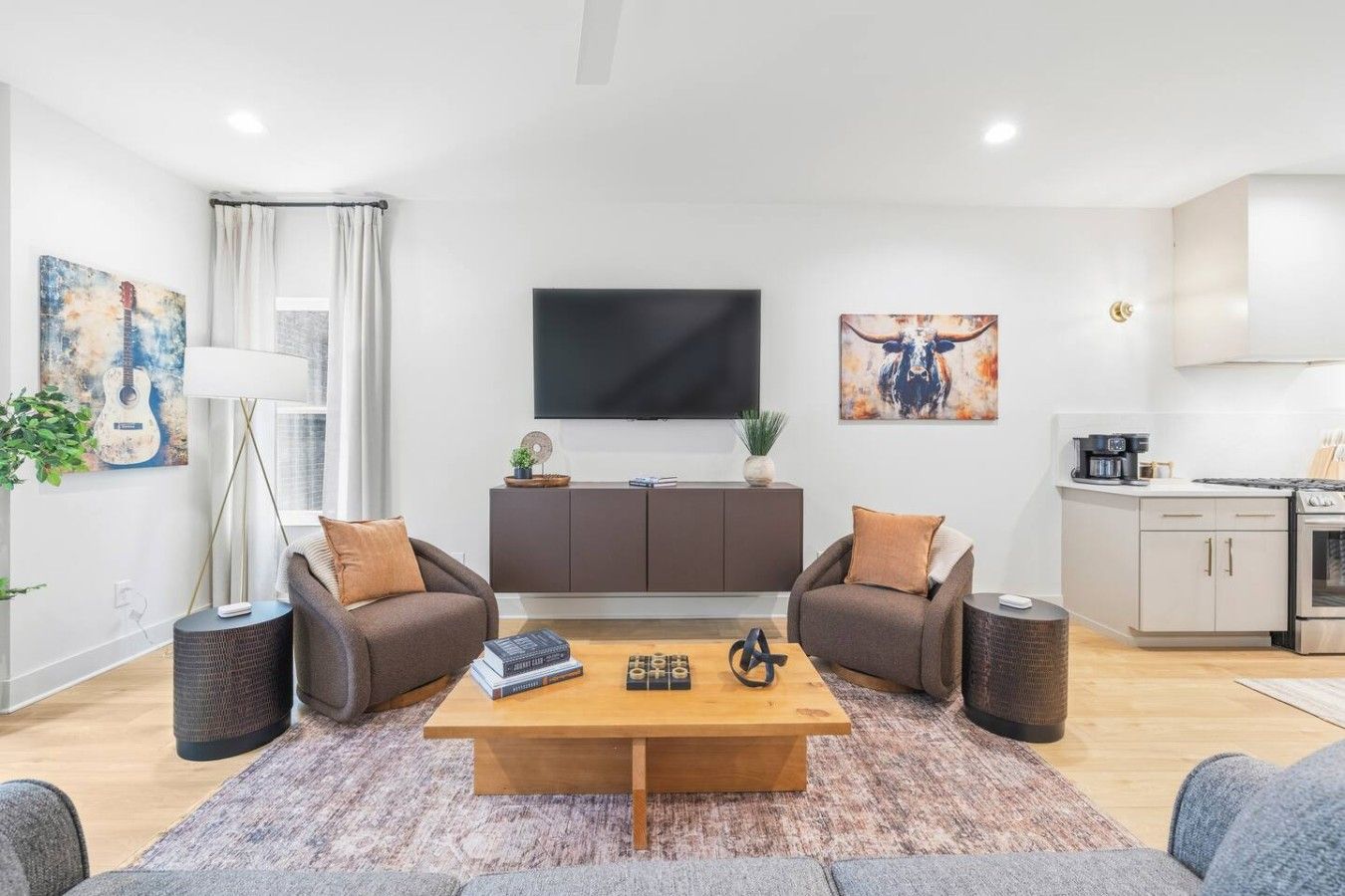 A modern living room with a flat-screen TV, two sofas, a coffee table, and a kitchen area with a stove.