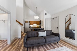 A modern interior with a grey sofa, wooden flooring, a kitchen with wooden cabinets, and a staircase.