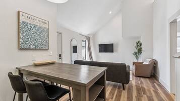 Una sala de estar moderna con una mesa de comedor de madera, sillas negras, un sofá gris y un televisor montado en la pared.