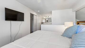 A hotel room with a bed, a TV mounted on the wall, a mirror above the bed, and a door leading to a bathroom.