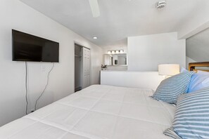 A hotel room with a bed, a TV mounted on the wall, a mirror above the bed, and a door leading to a bathroom.