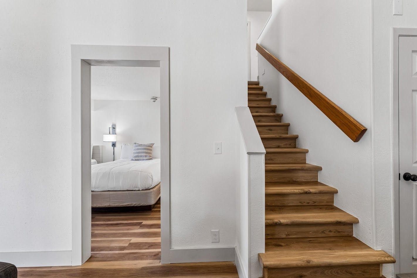 Una scala con gradini in legno e una ringhiera che conduce a una camera da letto con un letto e un comodino.