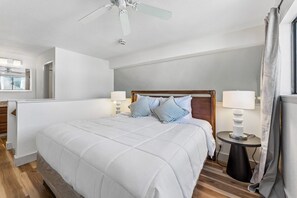 Habitación de hotel con una cama, lámparas de noche, ventilador de techo y ventana con cortinas.