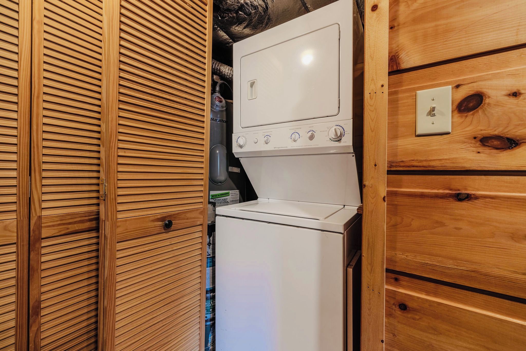 Une petite buanderie avec un lave-linge et un sèche-linge blancs, des murs recouverts de panneaux en bois et une petite prise électrique.
