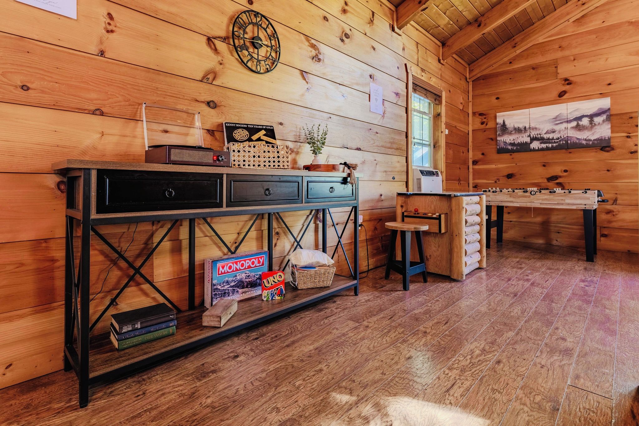 A wooden interior with a table, a clock, and a painting.