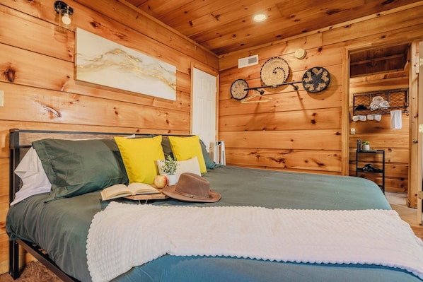 A wooden cabin bedroom with a bed, pillows, a hat, and a book.