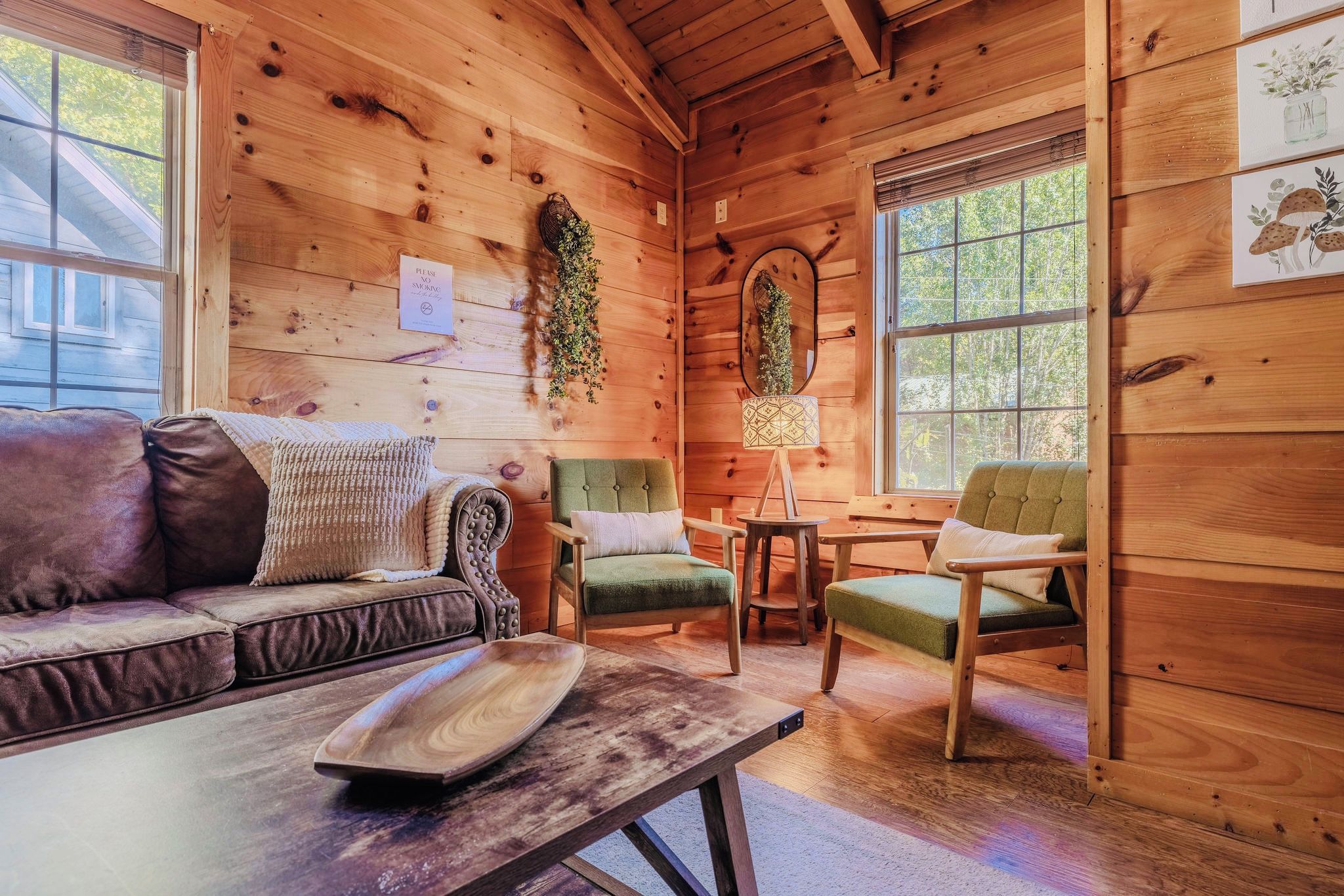 A cozy cabin interior with a wooden floor, a sofa, two chairs, a small table, and a lamp.