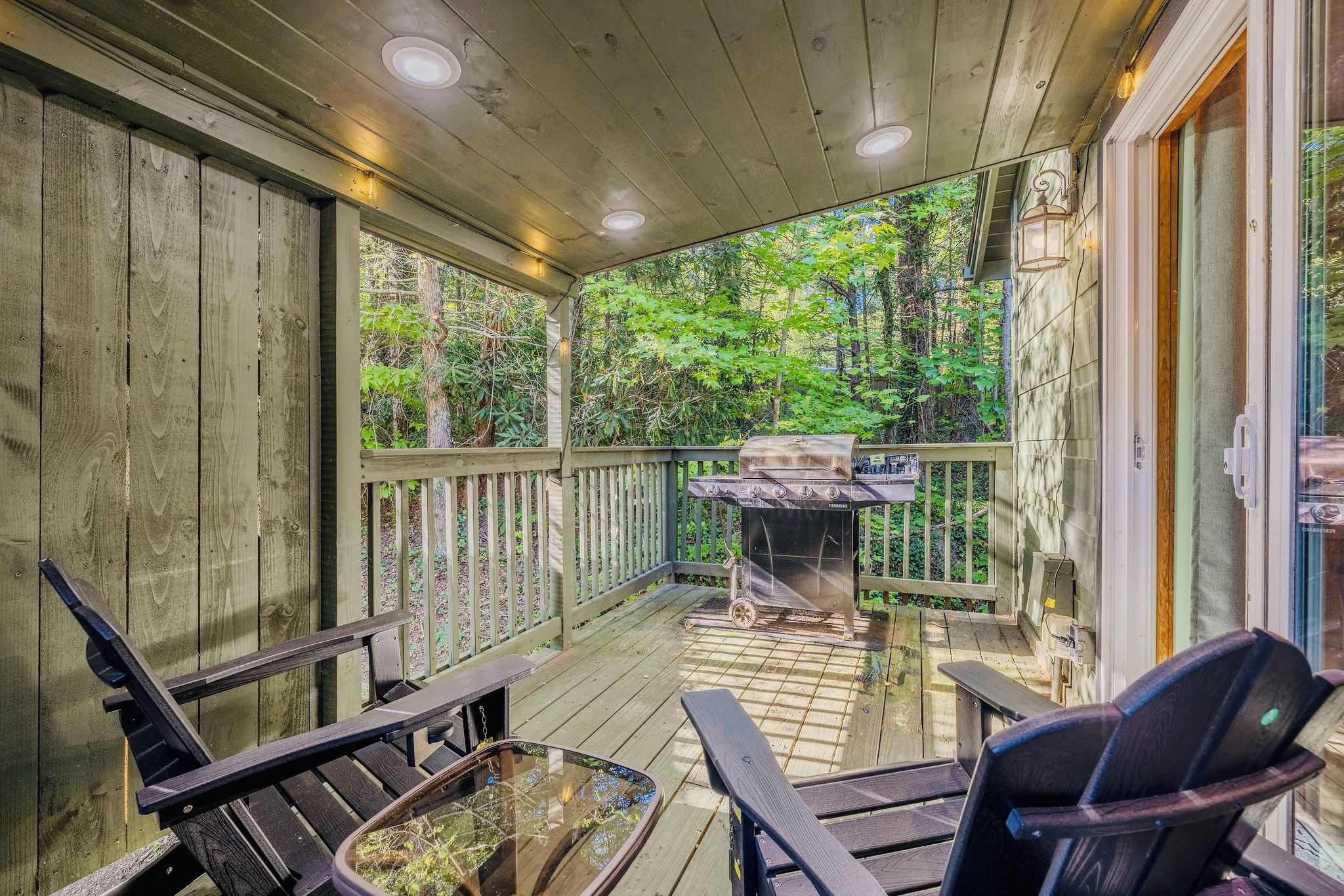 Une terrasse couverte avec des rampes en bois, un barbecue et des sièges d’extérieur.