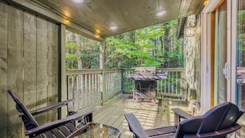 Une terrasse couverte avec des rampes en bois, un barbecue et des sièges d’extérieur.