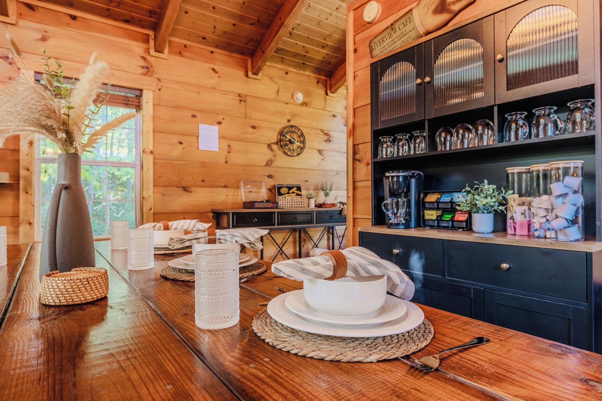 Un interno in legno con un tavolo da pranzo imbandito per due, una macchina per caffè e uno scaffale con barattoli e contenitori.