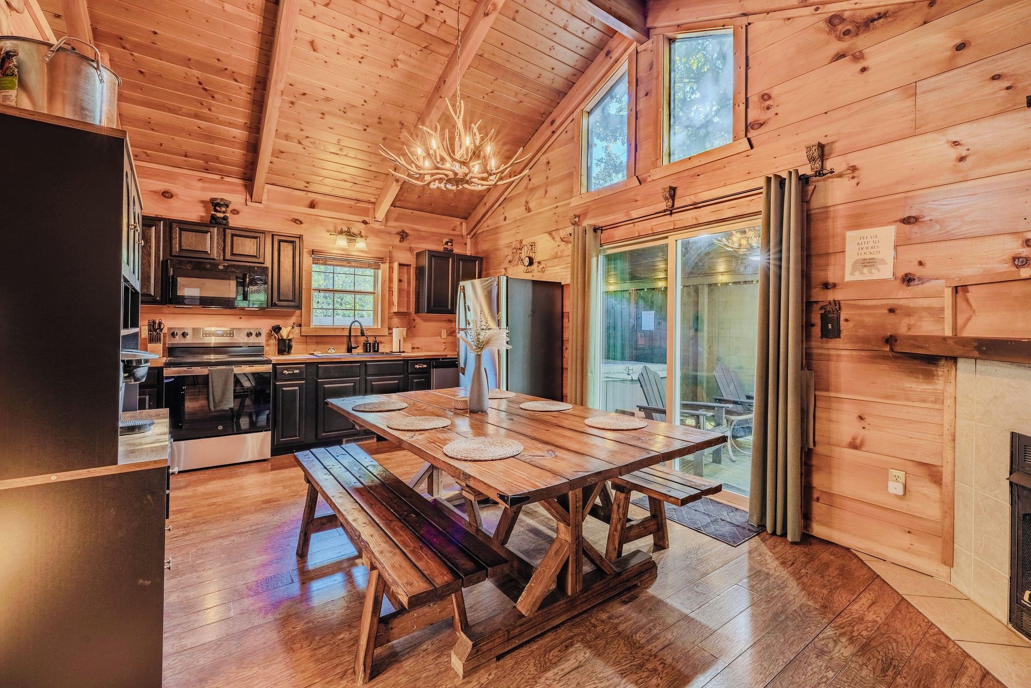 A wooden cabin interior with a dining table, kitchen area, and a chandelier.