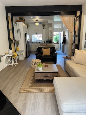 A modern living room with a black leather sofa, a beige sofa, and a coffee table with a plant. A kitchen is visible in the background with white cabinets and a microwave. - A Little Coastal Living_ Carlsbad Staycation (Carlsbad)