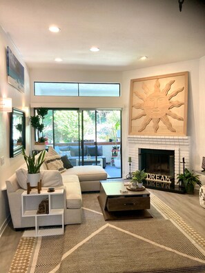 A modern living room with a fireplace, a large window, and a view of the outdoors. - A Little Coastal Living_ Carlsbad Staycation (Carlsbad)