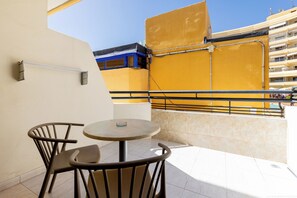 A balcony with a round table and two chairs, a yellow awning, and a building with balconies in the background. - Great Location Santa Maria, Costa Adeje (Costa Adeje)