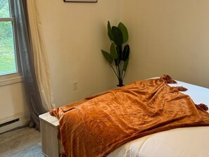 Ein Schlafzimmer mit einem Bett, einem Fenster mit Vorhängen, einer Pflanze und einer Heizung.