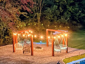 Two wooden swing chairs with string lights, a fire pit, and a garden setting at night. - Jamesville Luxury Retreat Pool, Hot Tub & 4BR (Jamesville)