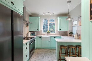 Une cuisine avec des meubles de couleur turquoise, un réfrigérateur en acier inoxydable, un four encastré et une fenêtre donnant sur un paysage verdoyant.