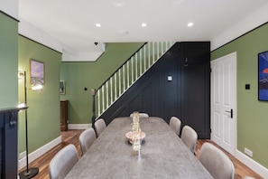 A dining area with a long table, chairs, a staircase, and a door. - The Tri-House (Watford)