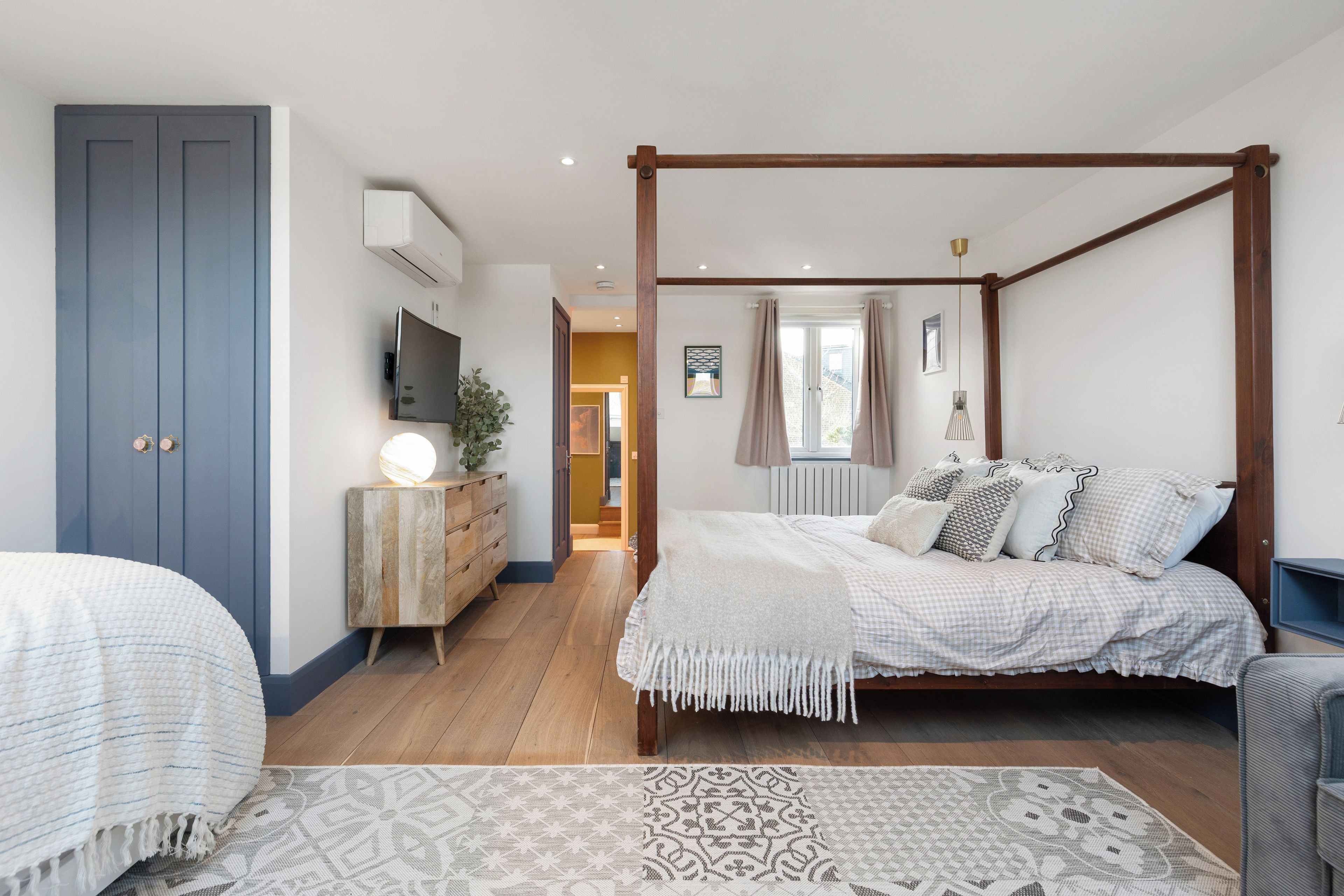 Een slaapkamer met een hemelbed, een dressoir, een televisie en uitzicht op een gang.
