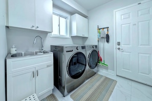A compact laundry room with a washing machine, a sink, and a drying rack. - Spacious 4-Bedroom Home Sleeps 8 Backyard (Barrie)