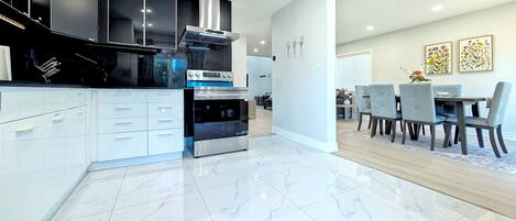 A modern kitchen with white cabinetry, a built-in oven, and a dining area with a table and chairs.