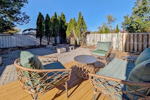 An outdoor patio with wicker furniture, a round table, and a wooden deck. - Spacious 4-Bedroom Home Sleeps 8 Backyard (Barrie)