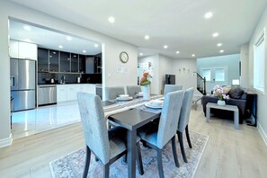 A modern kitchen with stainless steel appliances, a dining area with a table set for four, and a living room with a sofa and a coffee table. - Spacious 4-Bedroom Home Sleeps 8 Backyard (Barrie)