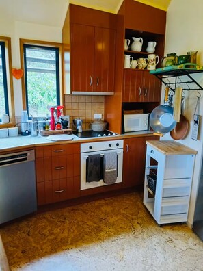 Een kleine keuken met houten kastjes, een magnetron, een fornuis en een hangende kookrek.