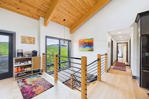 Ein modernes Interieur mit Holzboden, einer Treppe mit Metallgeländer, einer Küchenzeile und Blick ins Freie.