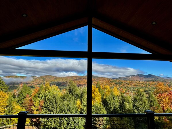 A view through a large window with a wooden frame, overlooking a forested landscape with autumn foliage and distant hills. - Shimmering Peaks Retreat (Thornton)
