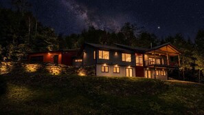 A two-story house with a balcony, surrounded by trees, under a starry night sky. - Shimmering Peaks Retreat (Thornton)