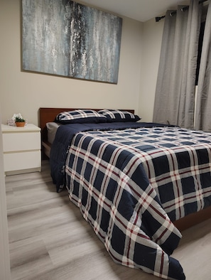 A bedroom with a bed, a nightstand, a potted plant, and a painting on the wall. - Cozy 3-bedroom House Rental in Calgary's Rosscarrock Area (Calgary)