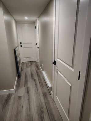 A hallway with wooden flooring, white walls, and doors. - Cozy 3-bedroom House Rental in Calgary's Rosscarrock Area (Calgary)