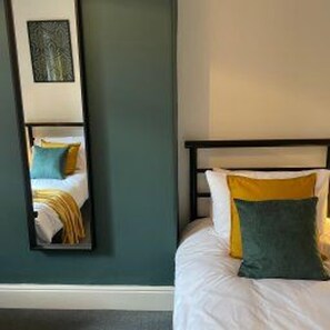 A bed with white bedding and two pillows, one yellow and one green, in a room with teal walls. - Central Darlington - House - Parking - Sleeps 5 (Darlington)