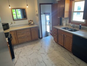 A kitchen with wooden cabinets, a marble floor, a microwave, and a sink. - Family Home with Large Kitchen & Sun Porch (Erie)