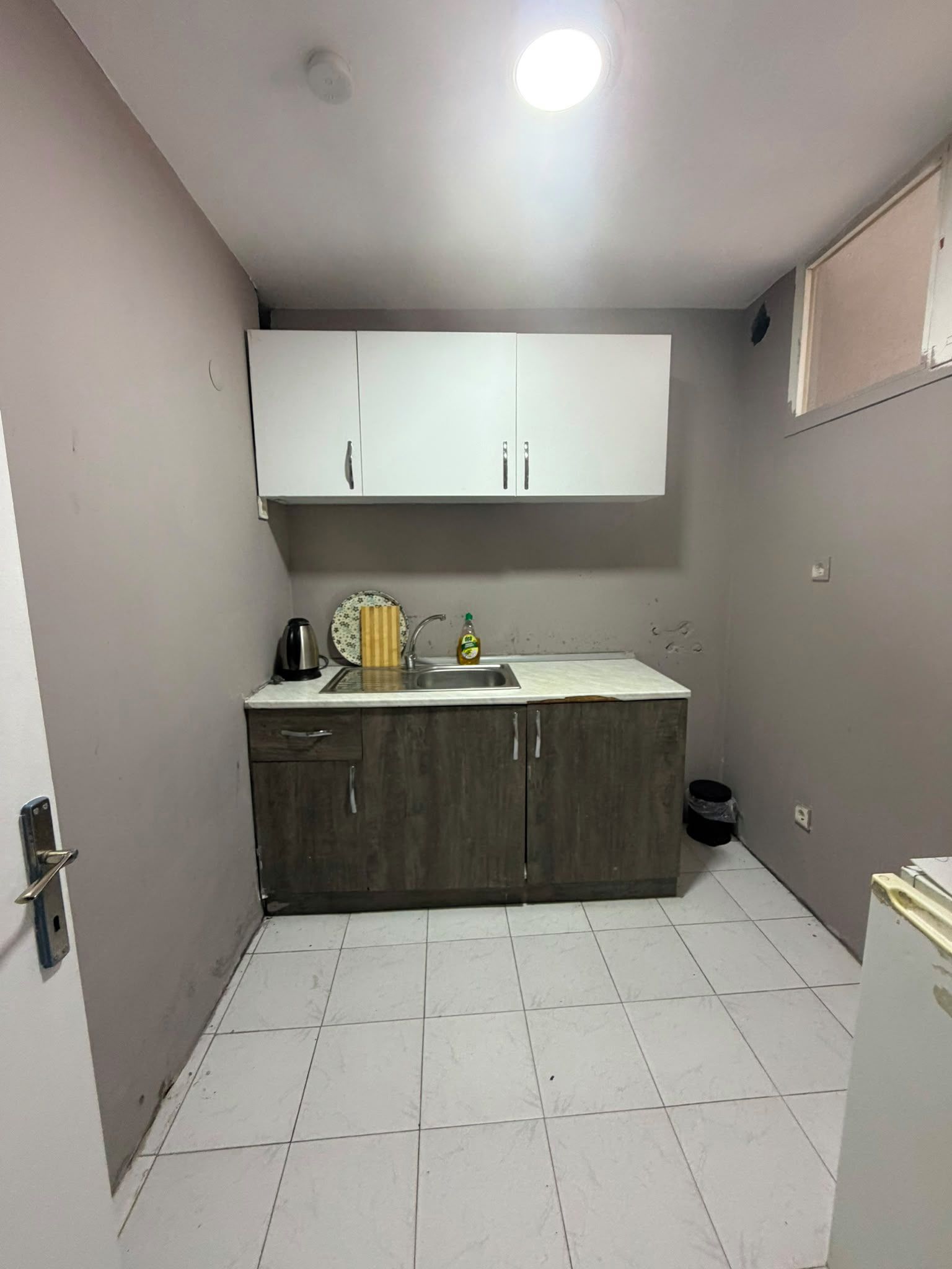 Una cocina pequeña con gabinetes blancos, un fregadero y piso de baldosas.