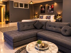 Una sala moderna con un sofá modular, una mesa de centro redonda con una planta y una cama con almohadones estampados.