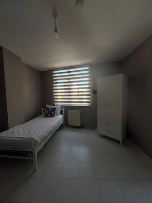 Un dormitorio con cama, radiador, armario y ventana con persianas.