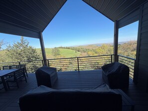 Un espace extérieur abrité, aménagé avec des sièges, et offrant une vue sur des collines verdoyantes et des arbres.