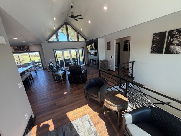 A spacious living area with a high ceiling, a ceiling fan, and a view through large windows to the outdoors.