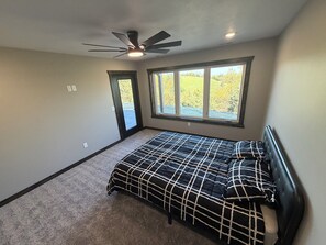 Un dormitorio con cama, ventilador de techo, ventana con vistas a la vegetación y puerta que da al exterior.