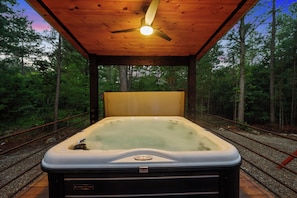 A hot tub in a forested area with a wooden deck and a ceiling fan. - Hot Tub | Game Room | Playset | Patio Oasis! (Broken Bow)