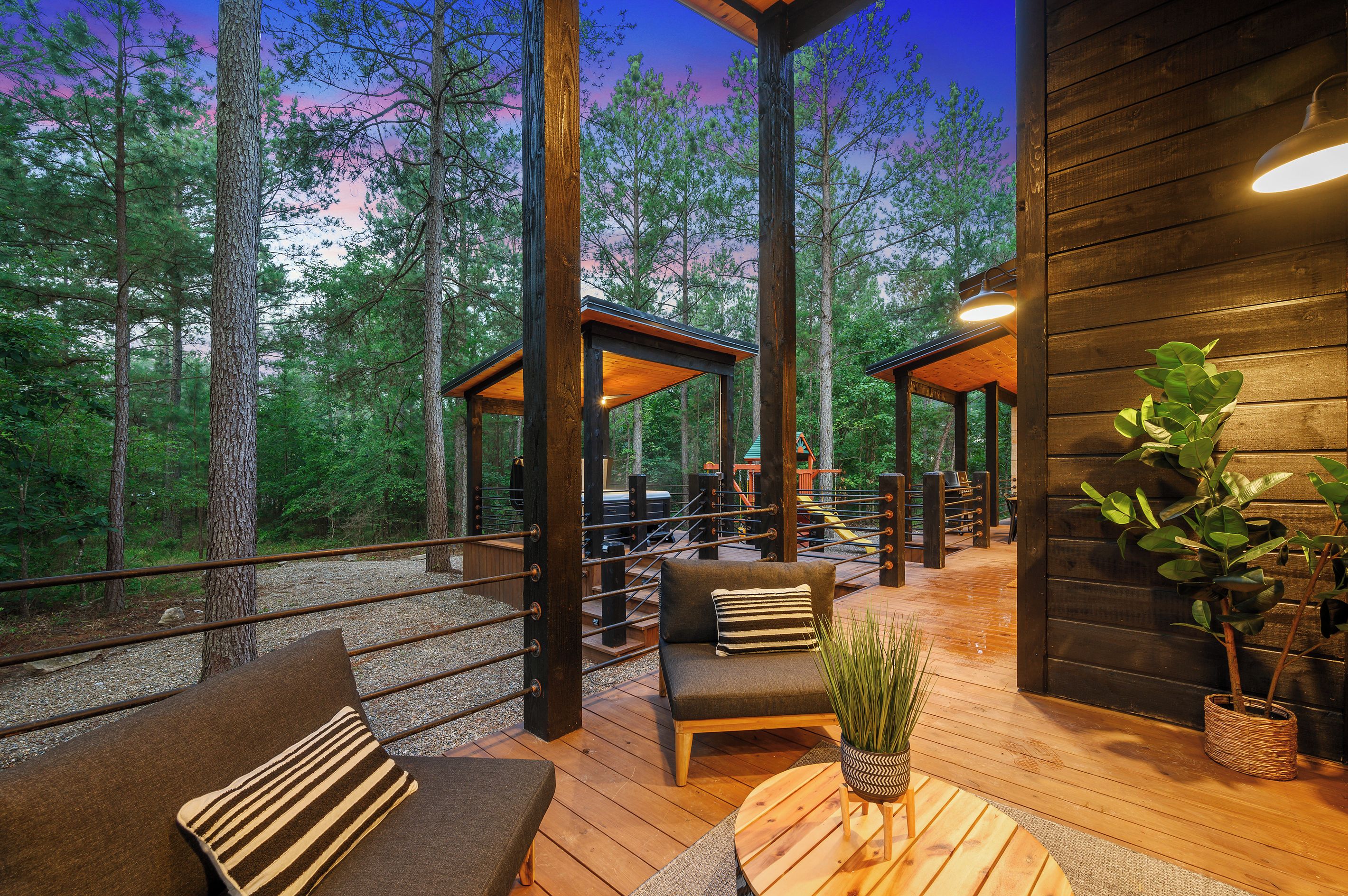 A wooden deck with outdoor seating, surrounded by tall trees, and a view of the forest.