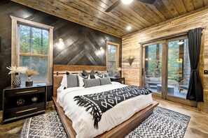 A bedroom with a large bed, a nightstand, a dresser, and a window with a view of trees. - Hot Tub | Game Room | Playset | Patio Oasis! (Broken Bow)