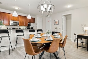 A modern kitchen with wooden cabinets, a central island, and a dining area with a round table and leather chairs. - Vista Cay 3BR Near Universal & Epic Universe (Orlando)